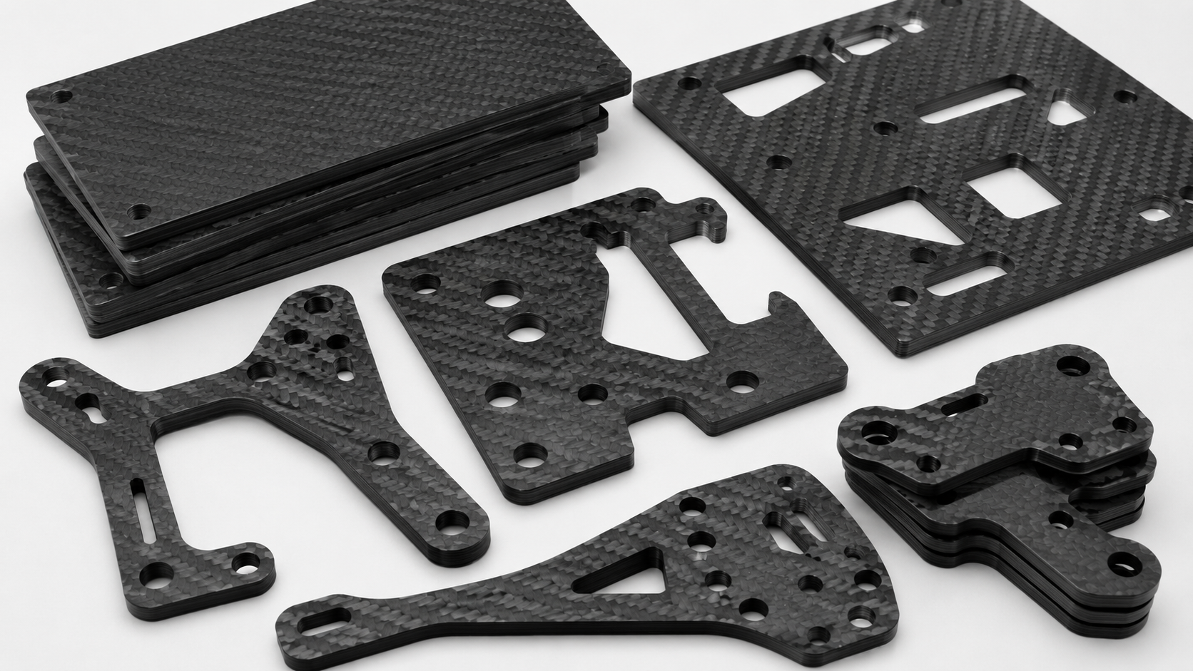 CNC-machined carbon fiber stock plates with holes, slots, clean edges and visible laminate layers.